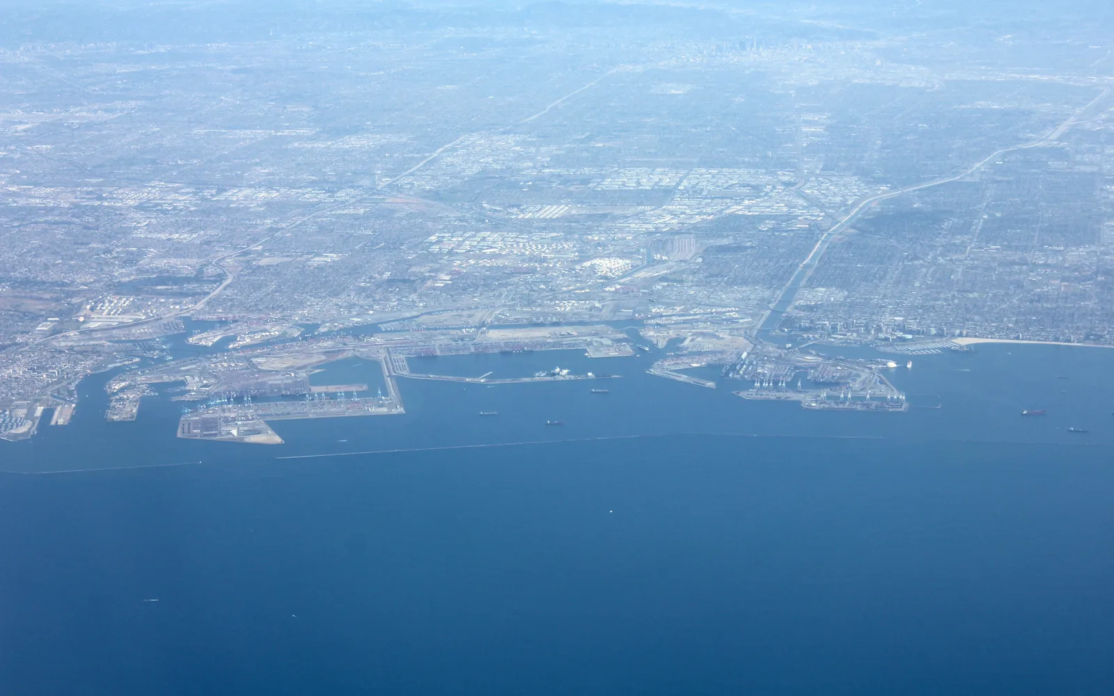 Aerial view of the Port of Los Angeles showing container ships, cranes, and stacked cargo containers with the harbor and surrounding industrial facilities